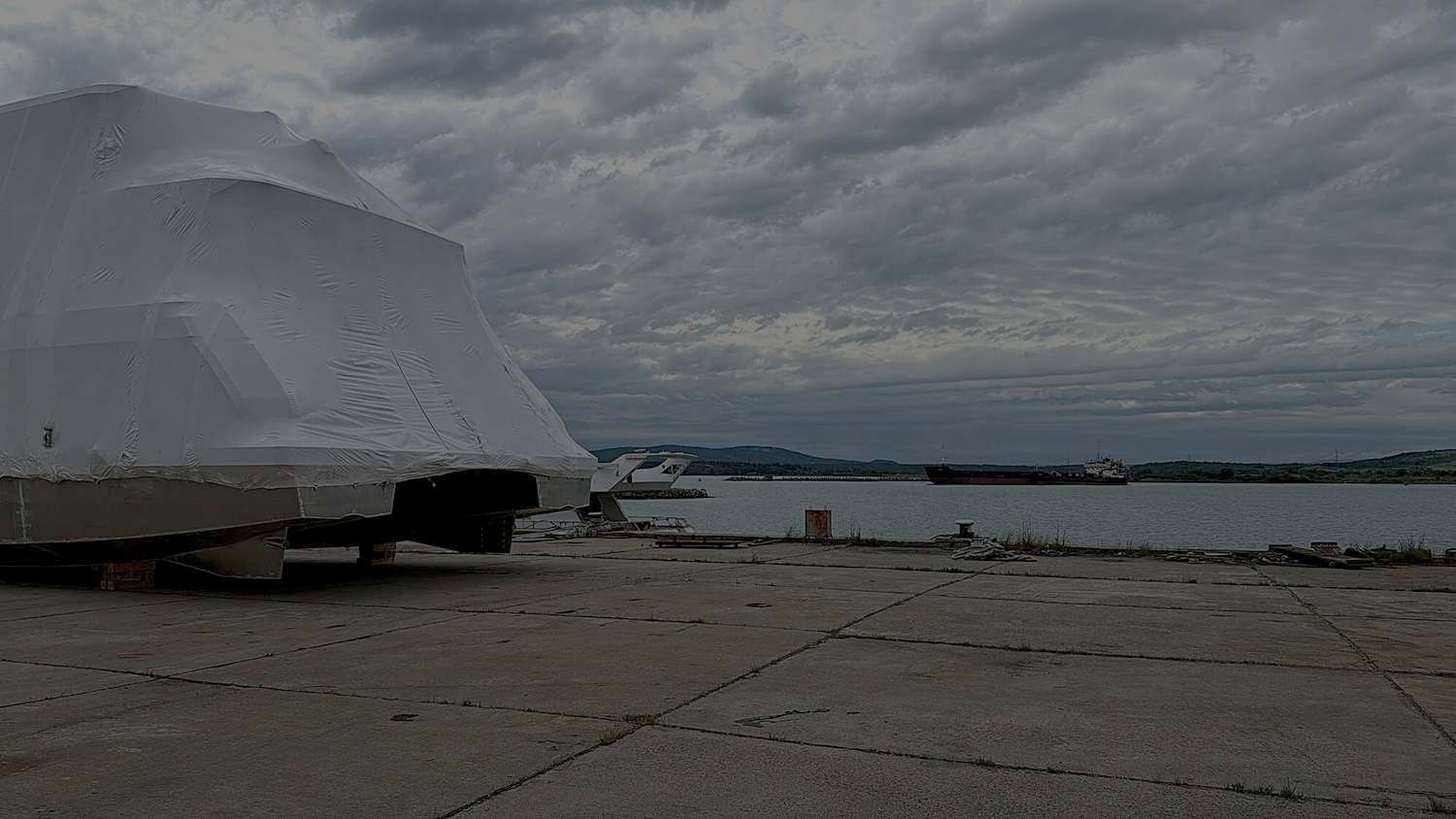 Shrink-wrapped hulls in winter storage on the concrete yard beside the water
